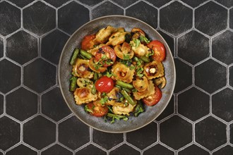 Overhead view of bowl with fried ravioli with string beans, tomato and mushrooms