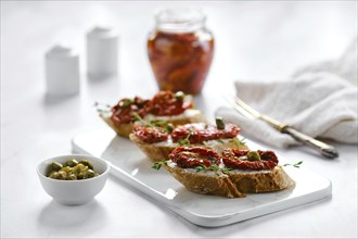 Baguette with sun-dried tomatoes and capers on marble serving board