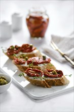 Bruschetta with sun-dried tomatoes and capers on marble serving board