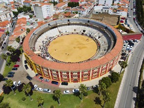 Historic bullring in a city, surrounded by buildings and green landscape, with cars and trees