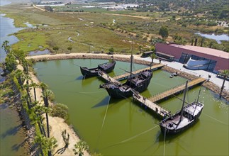 Historically modelled sailing ships in a calm water basin, surrounded by landscape under a clear