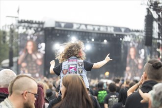 Toddler with metal cowl on his shoulders in front of the Faster stage at the Wacken Open Air in