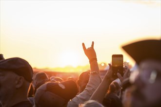 Metal greeting in front of the setting sun at the Wacken Open Air in Wacken. The traditional metal