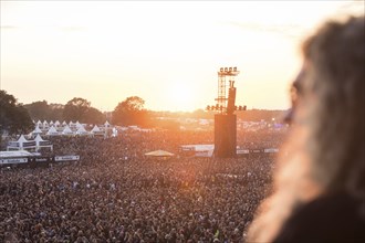 A man with long hair looks from an elevated position at the crowd with the setting sun at the