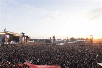 Overview of the crowd with the setting sun and the two main stages Faster and Harder at the Wacken