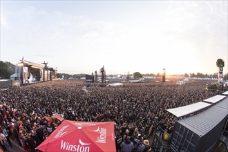 Overview of the crowd with the setting sun and the two main stages Faster and Harder at the Wacken