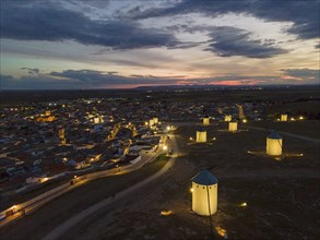 Illuminated windmills and a village in the light of dusk. The sky shows bright colours of the