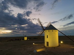 An illuminated windmill at night under a cloudy sky. The surroundings appear calm and quiet, while