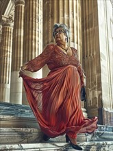 Statuesque woman in an elegant red dress, poised gracefully on a grand marble staircase with