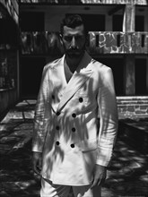 Man in a double-breasted white suit standing in strong shadows, evoking a classic and serious