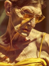 Old man with yellow sunglasses and outfit, showcasing deep wrinkles and a serious expression in