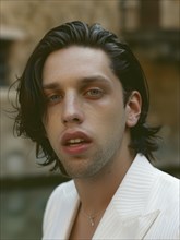 A close-up of a young man in a white jacket, looking introspective with natural light highlighting