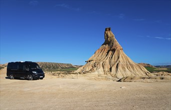 Motorhome in a barren desert landscape with striking rock formations and a clear blue sky,