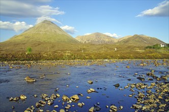 Landscape with mountains in the background, a shallow river full of stones and a clear blue sky