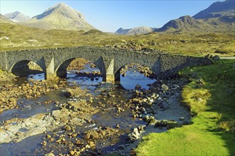 Historic stone bridge over a shallow river with mountains in the background, Slicgachan, Isle of