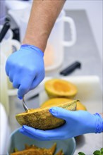 Person scooping cantaloupe with a spoon in the kitchen, emphasizing food preparation, hand hygiene,