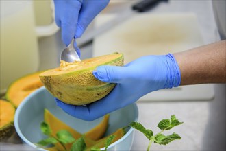 Person preparing cantaloupe with a spoon in the kitchen, highlighting food preparation, hand