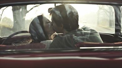 Couple in a vintage car kissing in the back seat with a serene nature background, AI generated