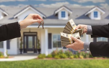 Real estate agent handing over house keys for stacks of money in front of new house