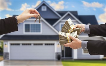 Real estate agent handing over house keys for stacks of money in front of new house