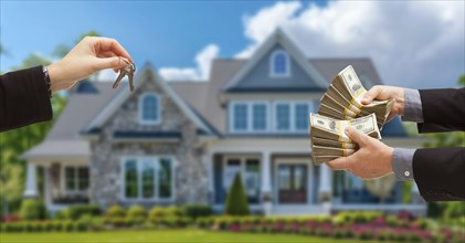 Real estate agent handing over house keys for stacks of money in front of new house