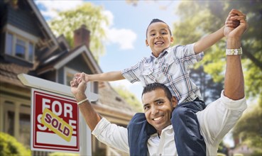 Happy father and son riding piggyback in front of new house and sold for sale real estate sign