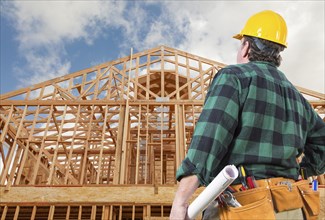 Contractor wearing hard hat standing in front of new house wood framing at construction site