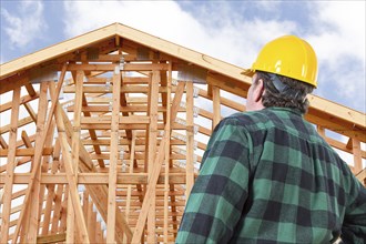 Contractor wearing hard hat standing in front of new house wood framing at construction site