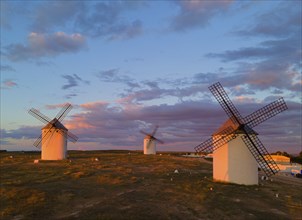 Three windmills stand on a vast landscape under a pink and blue sky during sunset, aerial view,