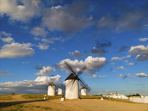 White windmills under a blue, slightly cloudy sky, with a gravel path next to them, windmills,