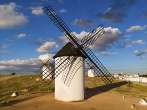 White windmills in the sun under a blue sky with clouds, surrounded by an open landscape, aerial