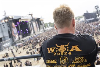 A festival visitor with a W:O:A 2024 T-shirt looks at the two main stages at the Wacken Open Air in