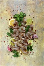 Raw shrimp on skewers, shrimp kebabs, slices of lime and lemon, spices and herbs, top view, without