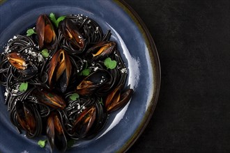 Spaghetti with black squid, black pasta, with boiled mussels, on a black plate, with parsley and