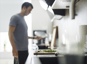 Cooking theme. A chopping board with parsley, in the background a man stands at the cooker and