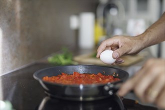 Cooking topic. A man cracks a raw egg into a pan. Berlin, 01.08.2024