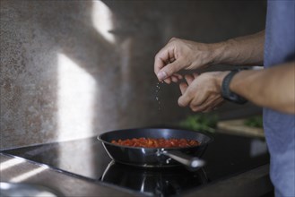 Cooking topic. A man salts a dish in a pan. Berlin, 01.08.2024