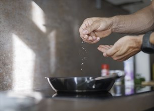 Cooking topic. A man salts a dish in a pan. Berlin, 01.08.2024