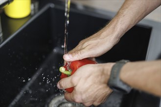 Cooking theme. A man washes a red pepper over a sink. Berlin, 01.08.2024