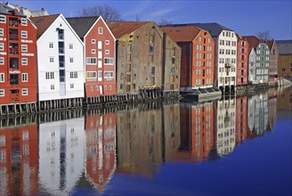 Row of colourful houses reflected in the water under a bright blue sky, Nidarelva, Trondheim,