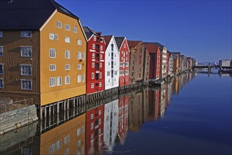 Colourful houses along a calm water with a clear reflection under a blue sky, Nidarelva, Trondheim,