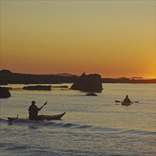 Two people kayaking on a calm water at sunset, Ramberg, Flakstad, Flakstadoya, Lofoten, Nordland,