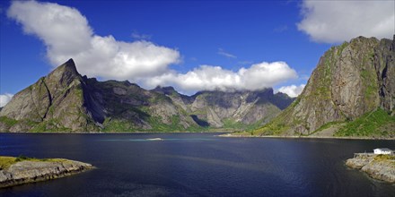 Impressive mountains under a blue sky with white clouds next to a calm fjord, Reinefjord, Hamnoy,