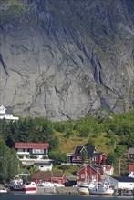 Idyllic fishing village with red house and fishing boats in front of an impressive rock face,