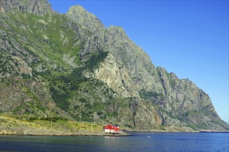 Secluded red cabin by the coast and steep green mountains under a clear sky, Rorbuer, holiday,