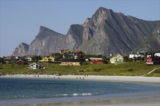 Small coastal village with colourful houses and beach, framed by majestic mountains under a clear