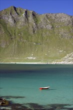 A red boat floats in a turquoise-coloured lake in front of a mountainous landscape, Haukland,