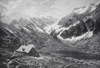 A small hut in a snowy valley, surrounded by high mountains, small pond in the Giant Mountains,