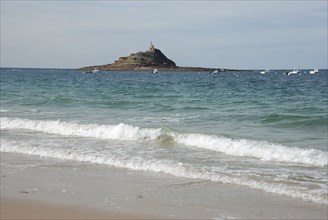 A lighthouse standing on an island surrounded by the ocean, with waves crashing on a sandy beach