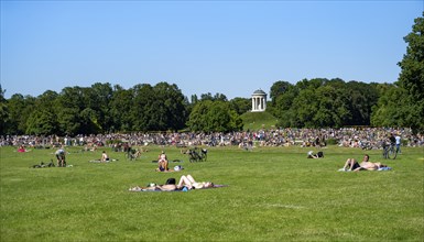 Many people in a meadow in the English Garden, people enjoying the summer day in the park behind